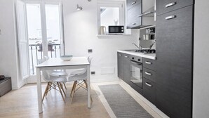 A modern kitchen with dark cabinets, a white countertop, and a microwave. There is a dining table with chairs and a bowl on it.