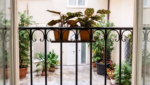 A balcony with potted plants, a small water feature, and a view of a building with windows and a door.
