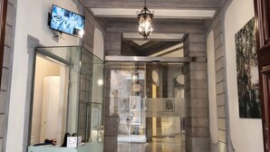 A hotel lobby with a reception desk, a chandelier, and a television mounted on the wall.