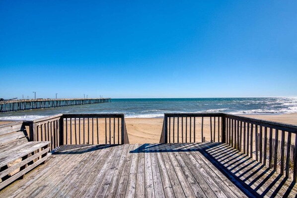A wooden pier leading to a beach with clear skies.