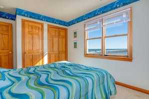 Une chambre à coucher avec un lit, des portes en bois, une fenêtre donnant sur un beau paysage et une couvre-lit aux motifs bleus et verts.