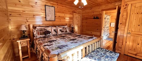 A wooden cabin bedroom with a bed, a bench, a ceiling fan, and a framed picture on the wall.