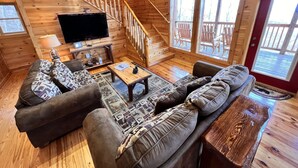 Ein gemütliches Blockhaushaus-Interieur mit einer Holztreppe, einem Fernseher, einer Couch und einem Couchtisch.
