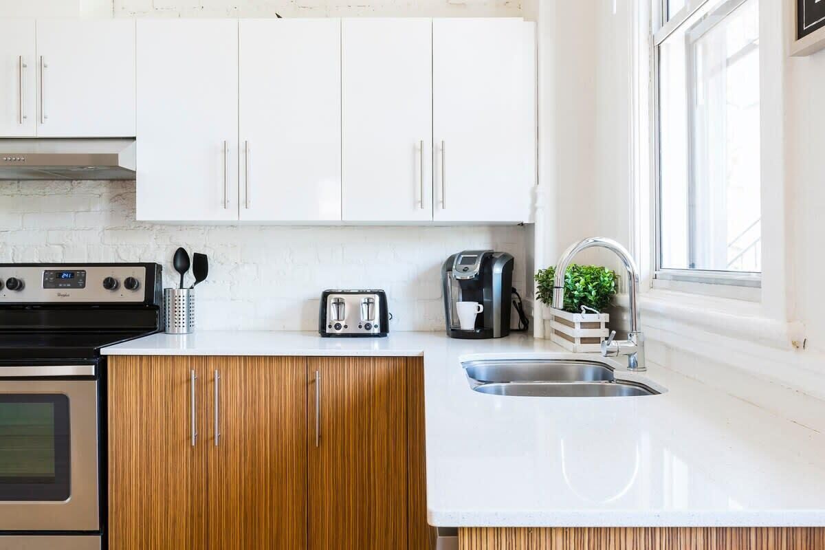 Een moderne keuken met witte kasten, een roestvrijstalen spoelbak, een broodrooster, een koffiezetapparaat en een raam dat natuurlijk licht binnenlaat.