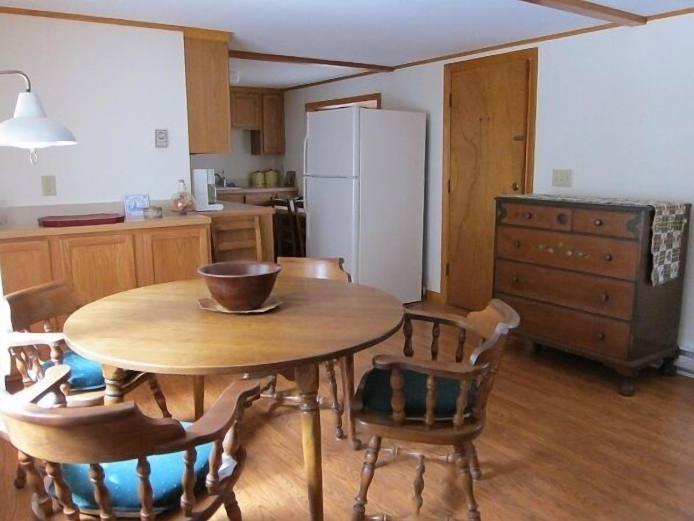 A compact kitchen with wooden cabinets, a white refrigerator, and a dining table with chairs.