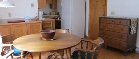 A compact kitchen with wooden cabinets, a white refrigerator, and a dining table with chairs.