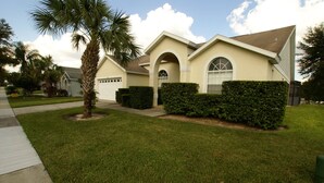 A residential house with a well-maintained lawn, a palm tree, and a garage. - Beautiful 4 Bed/3 Bath Villa + Disney&Golf + Large South-Facing private Pool/Spa (Clermont)