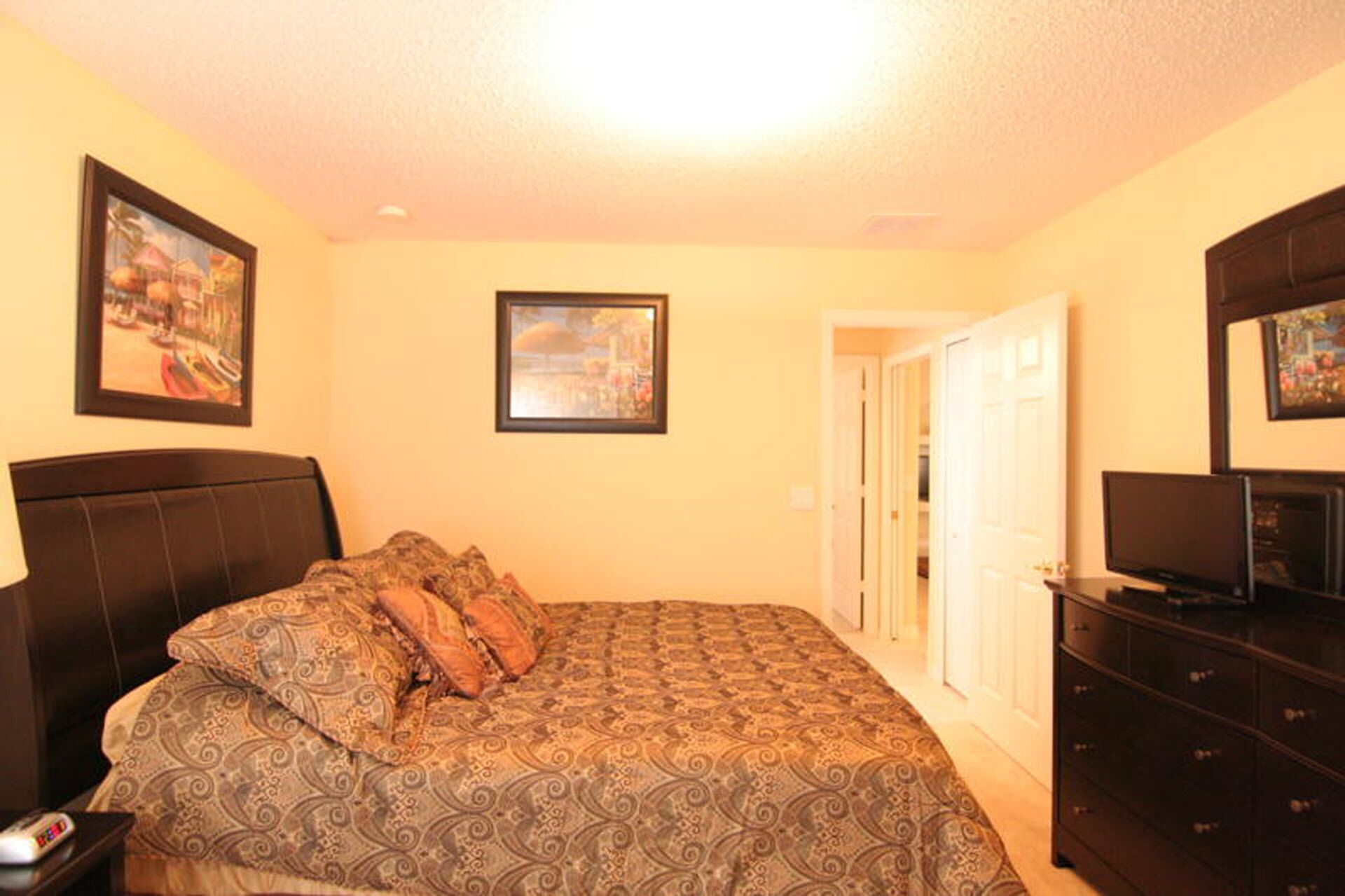 A bedroom with a bed, a TV, a dresser, and two framed pictures on the wall.