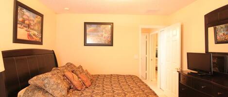 A bedroom with a bed, a TV, a dresser, and two framed pictures on the wall.