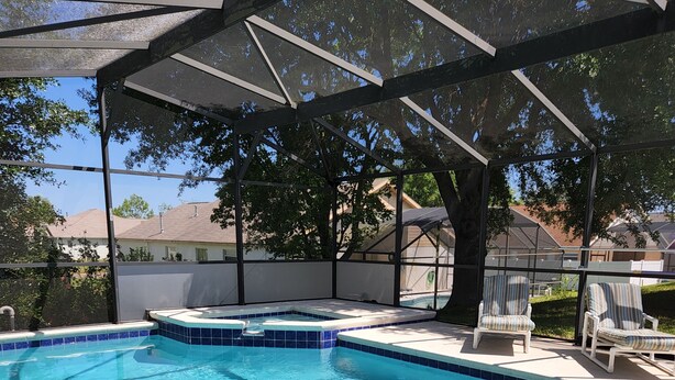 A clear swimming pool with a covered area, lounge chairs, and a view of the neighborhood. - Beautiful 4 Bed/3 Bath Villa + Disney&Golf + Large South-Facing private Pool/Spa (Clermont)