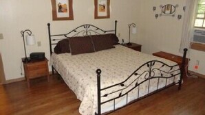A bedroom with a metal bed frame, a wooden nightstand, a bedside table, two framed pictures on the wall, and a window with curtains. - Mount Desert Island, Bar Harbor, Acadia National Park (Bar Harbor)