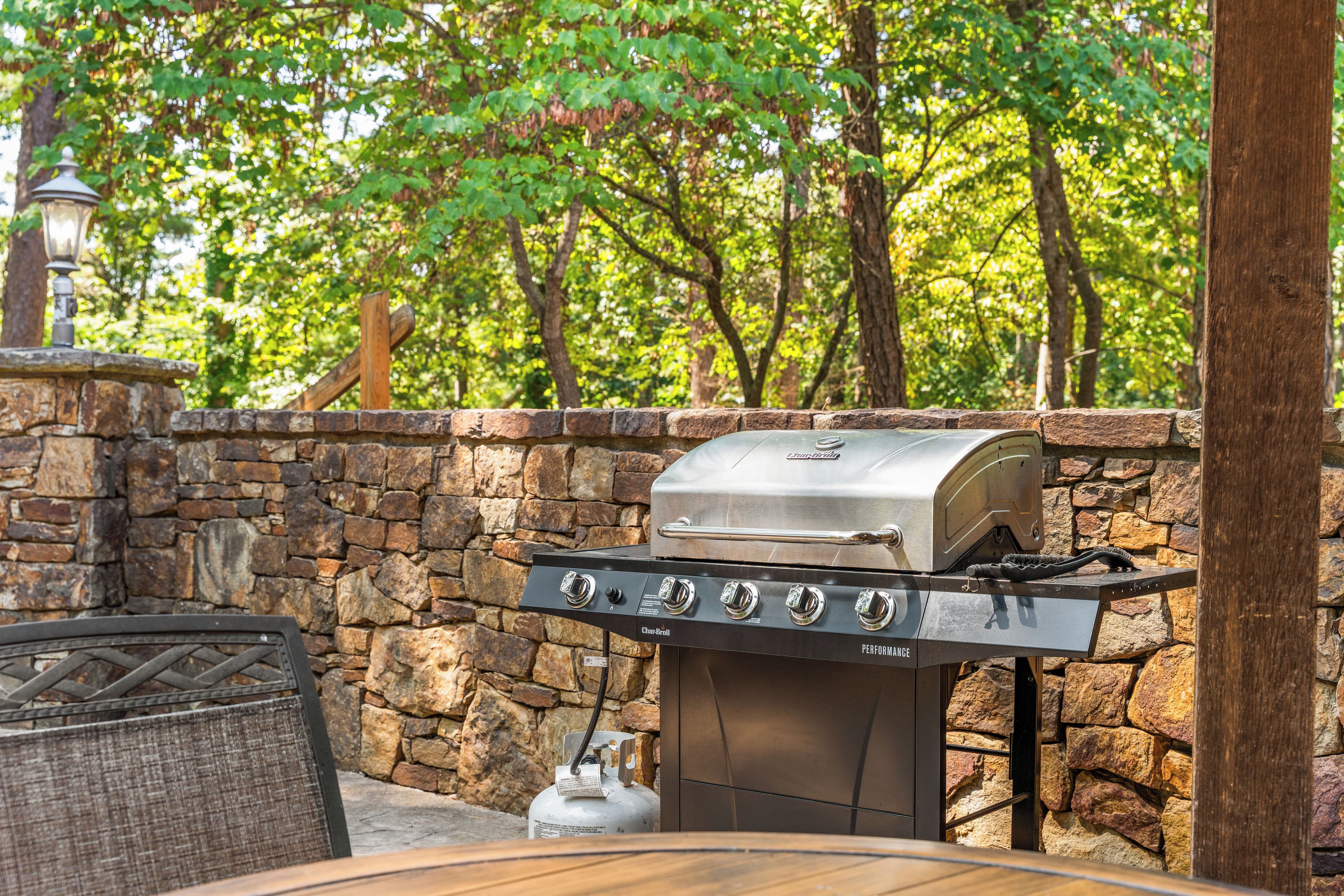 Un barbecue extérieur avec un mur en pierre en arrière-plan, une bouteille de gaz et une grille de cuisson en métal.