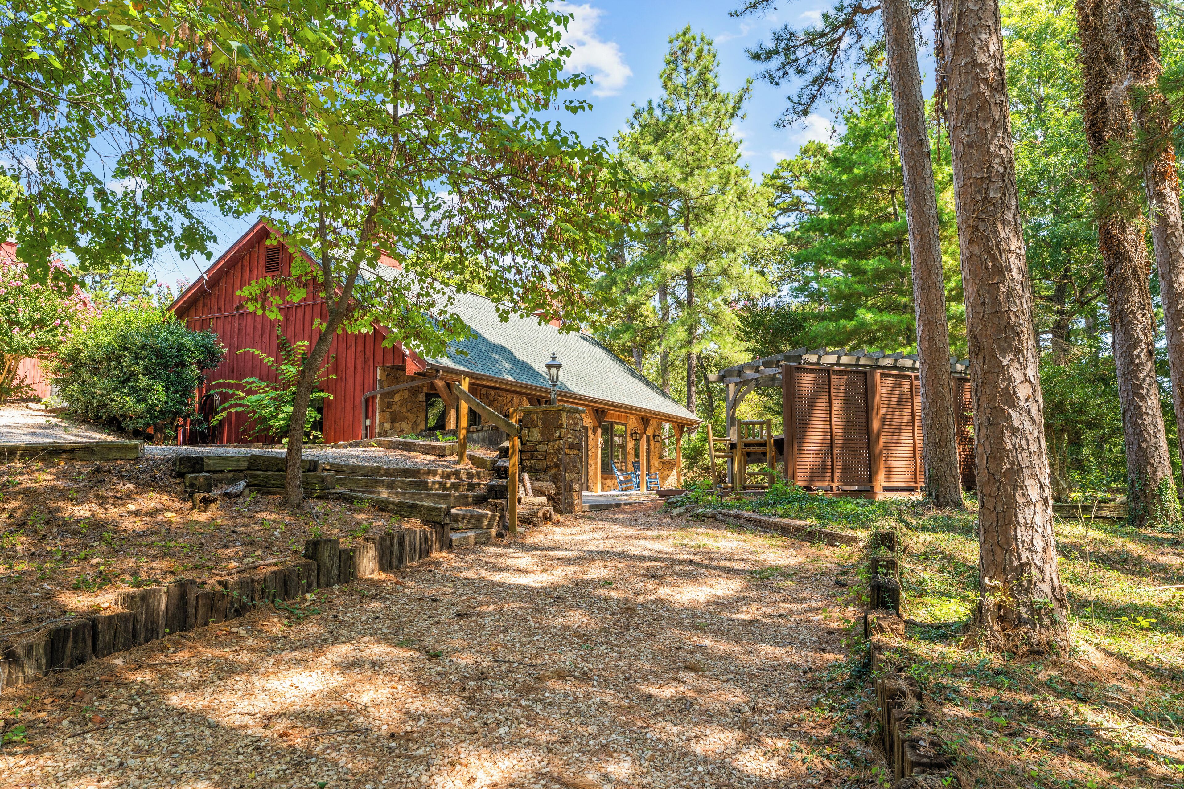 Une cabane rustique avec des fondations en pierre, une véranda en bois et, au loin, une grange rouge.
