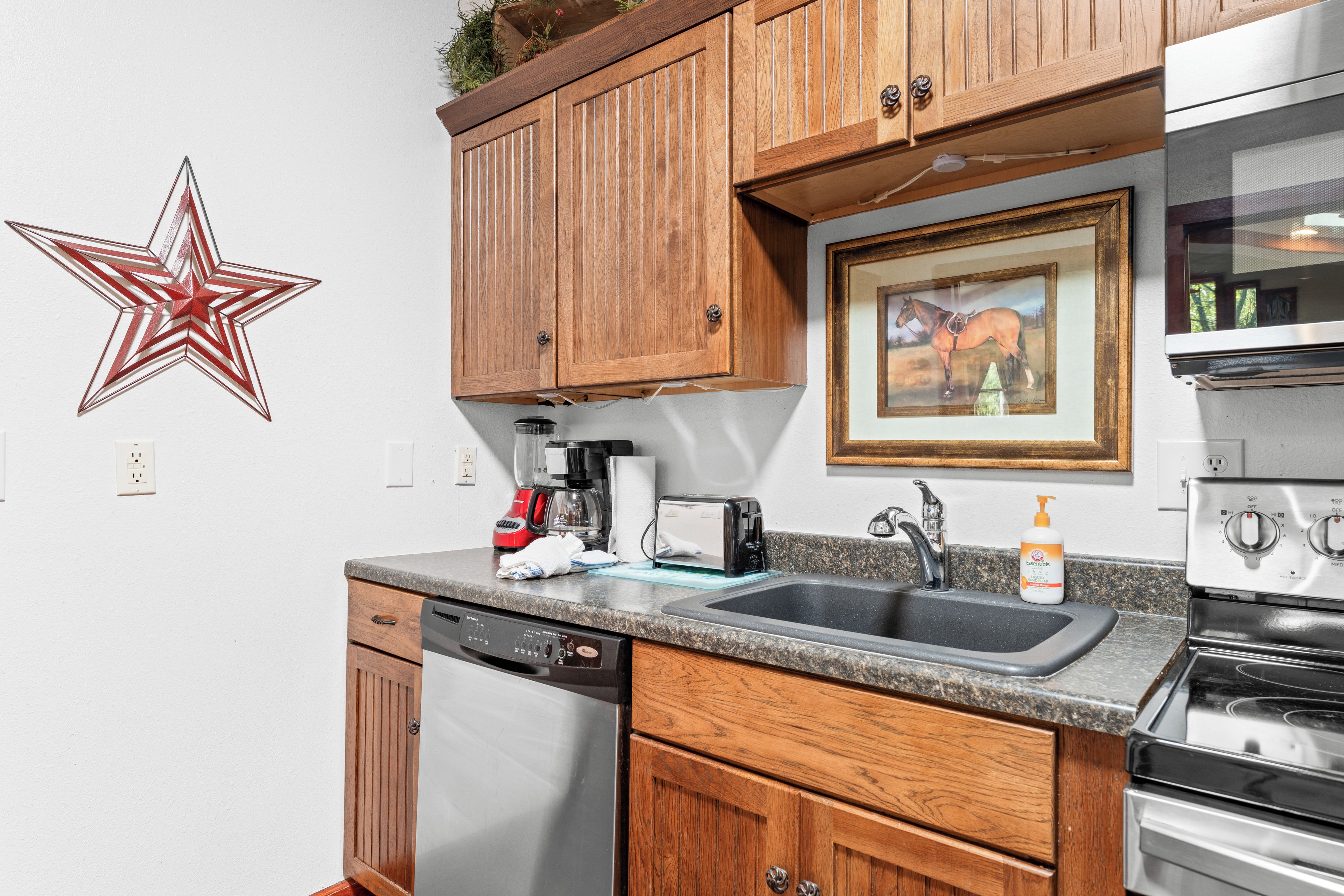 A kitchen with wooden cabinets, a dishwasher, a coffee maker, a toaster, a sink, and a framed picture on the wall.