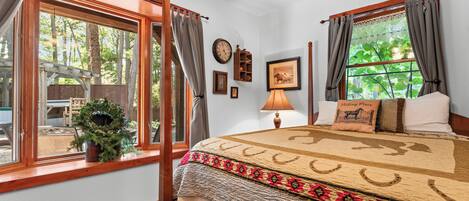 Une chambre avec une grande fenêtre, un lit recouvert d’une couvre-lit à motifs, une table de chevet, une lampe et une horloge murale.