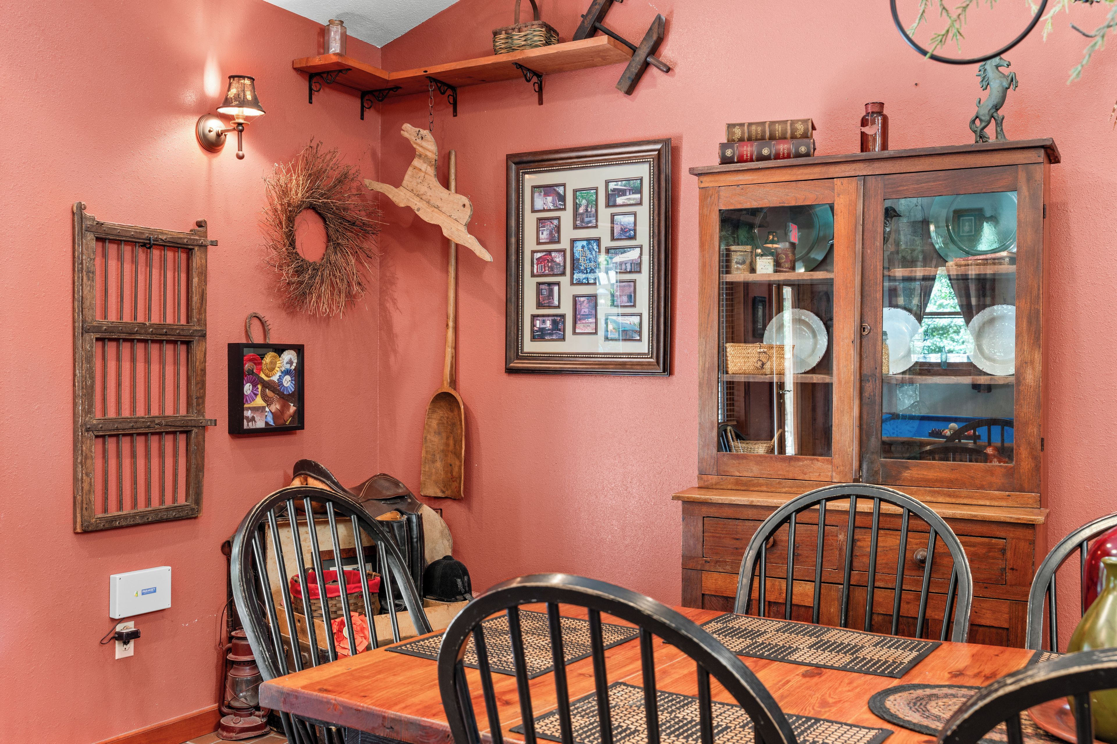 A dining area with a wooden table and chairs, a wall-mounted light fixture, and a framed collage of photographs.