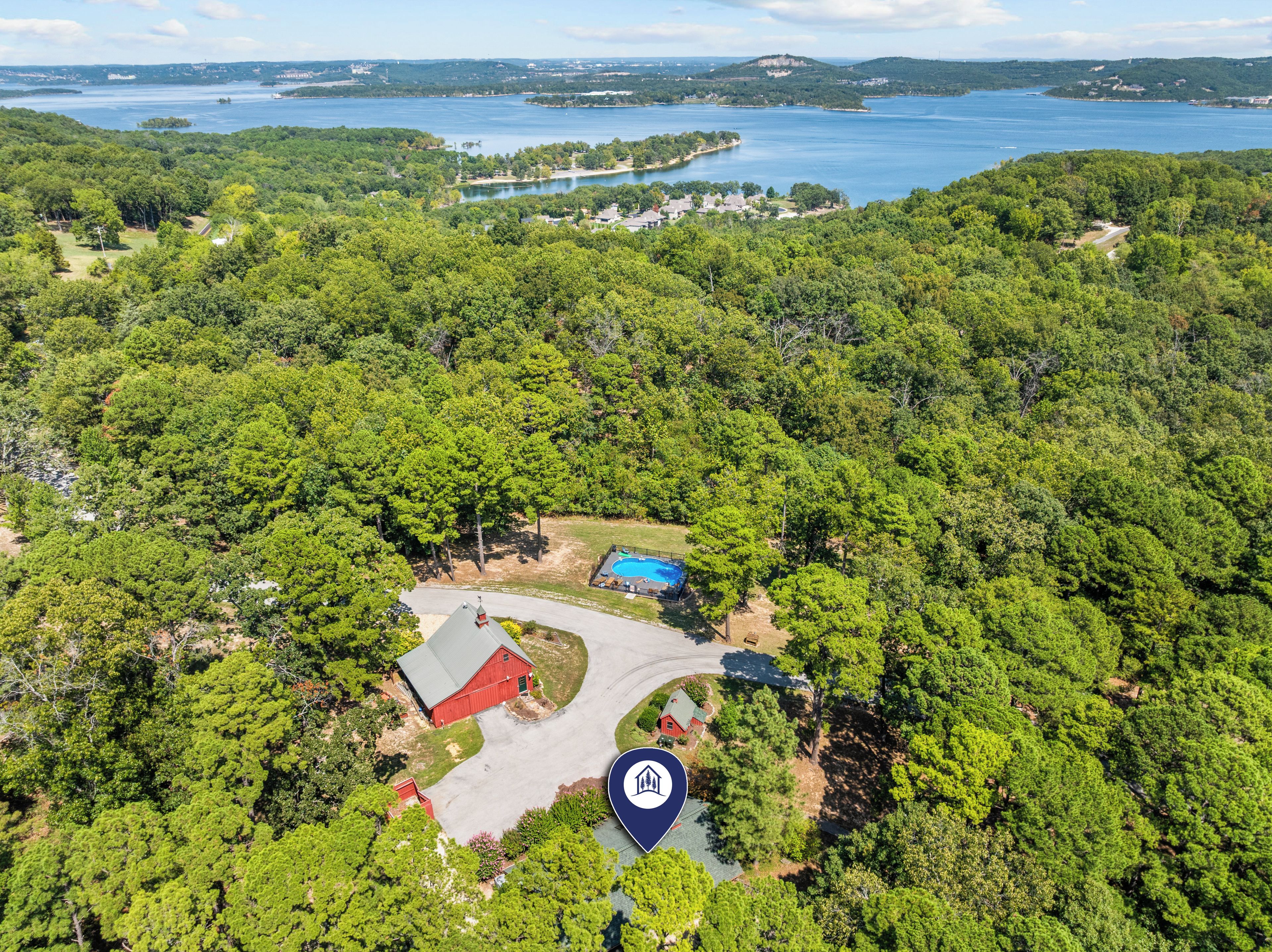 An aerial view of a property with a swimming pool, a red barn, and a large green forested area.
