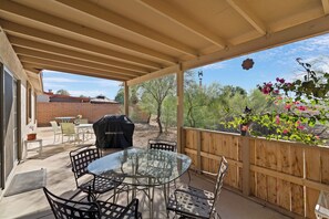 Une terrasse couverte avec une table et des chaises en verre, un barbecue et une clôture en bois.