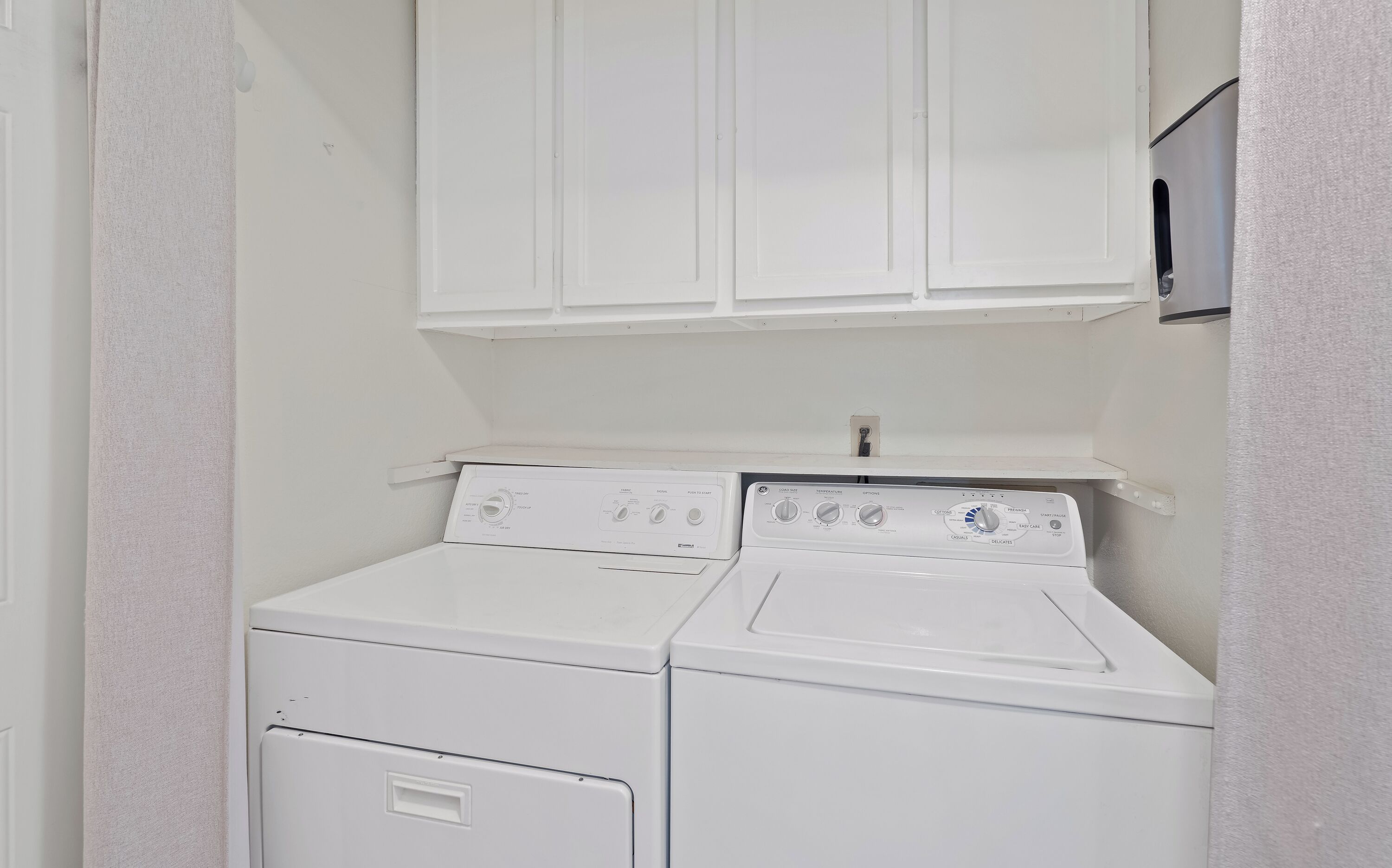 Une buanderie équipée de deux machines à laver et deux sèche-linge superposés, avec un meuble blanc au-dessus et une petite étagère.