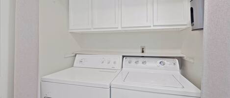 Une buanderie équipée de deux machines à laver et deux sèche-linge superposés, avec un meuble blanc au-dessus et une petite étagère.