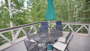 A covered outdoor deck with a round table and chairs, surrounded by a white railing.