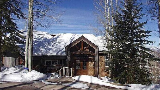 A wooden cabin with a stone foundation, surrounded by snow and trees.