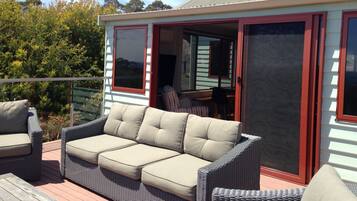 Een terras buiten met een rieten bank en stoelen, een schuifpui en uitzicht op de omliggende begroeiing.