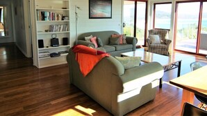 Un salon spacieux avec un canapé, une table basse et une bibliothèque. Une grande fenêtre offre une vue sur l’extérieur.
