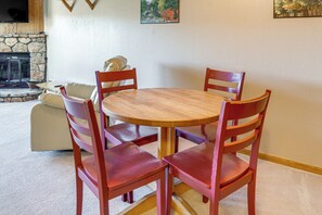 Een ronde houten tafel met vier rode stoelen, een stenen openhaard en een schilderij aan de muur.
