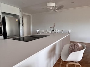 A modern kitchen with a central island, white chairs, and a ceiling fan.
