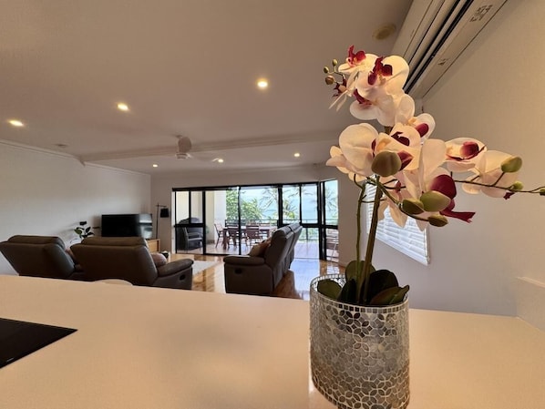 A modern living room with a white sofa, a coffee table, and a decorative orchid vase.