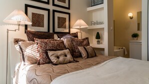Een netjes ingerichte slaapkamer met een groot bed, twee bedlampen, een klein plankje met decoratieve objecten en een wandlamp.
