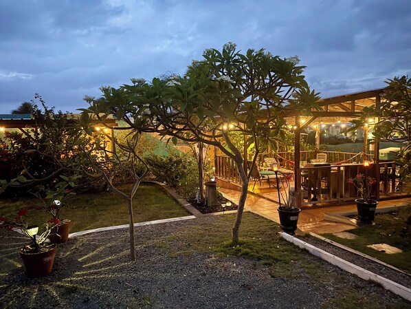 Área de terraço ao ar livre com pérgola de madeira, assentos e plantas em vasos.