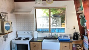 A kitchen with a stove, sink, and wooden cabinets. - Kiwi Bach by the Beach (Castle Point)