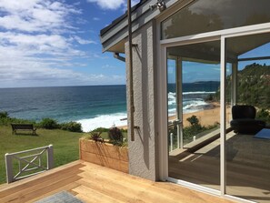 A modern house with a large glass door leading to a deck overlooking a beach. - Northern Beaches beachfront house . (Warriewood)