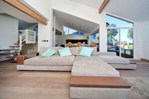 A modern living room with a large sectional sofa, wooden platform seating, and a view of the outdoor patio. - Northern Beaches beachfront house . (Warriewood)