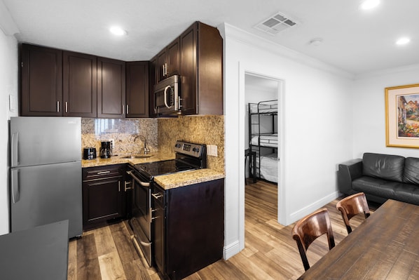 A compact kitchen with dark cabinets, a stainless steel microwave, and a granite countertop.