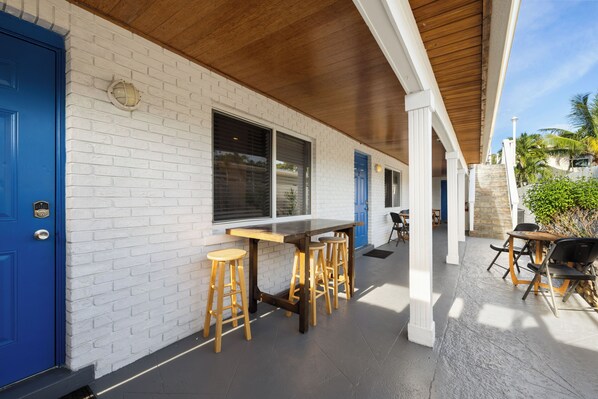 Un espacio al aire libre cubierto con pared de ladrillo blanco, puertas azules y mobiliario de madera.