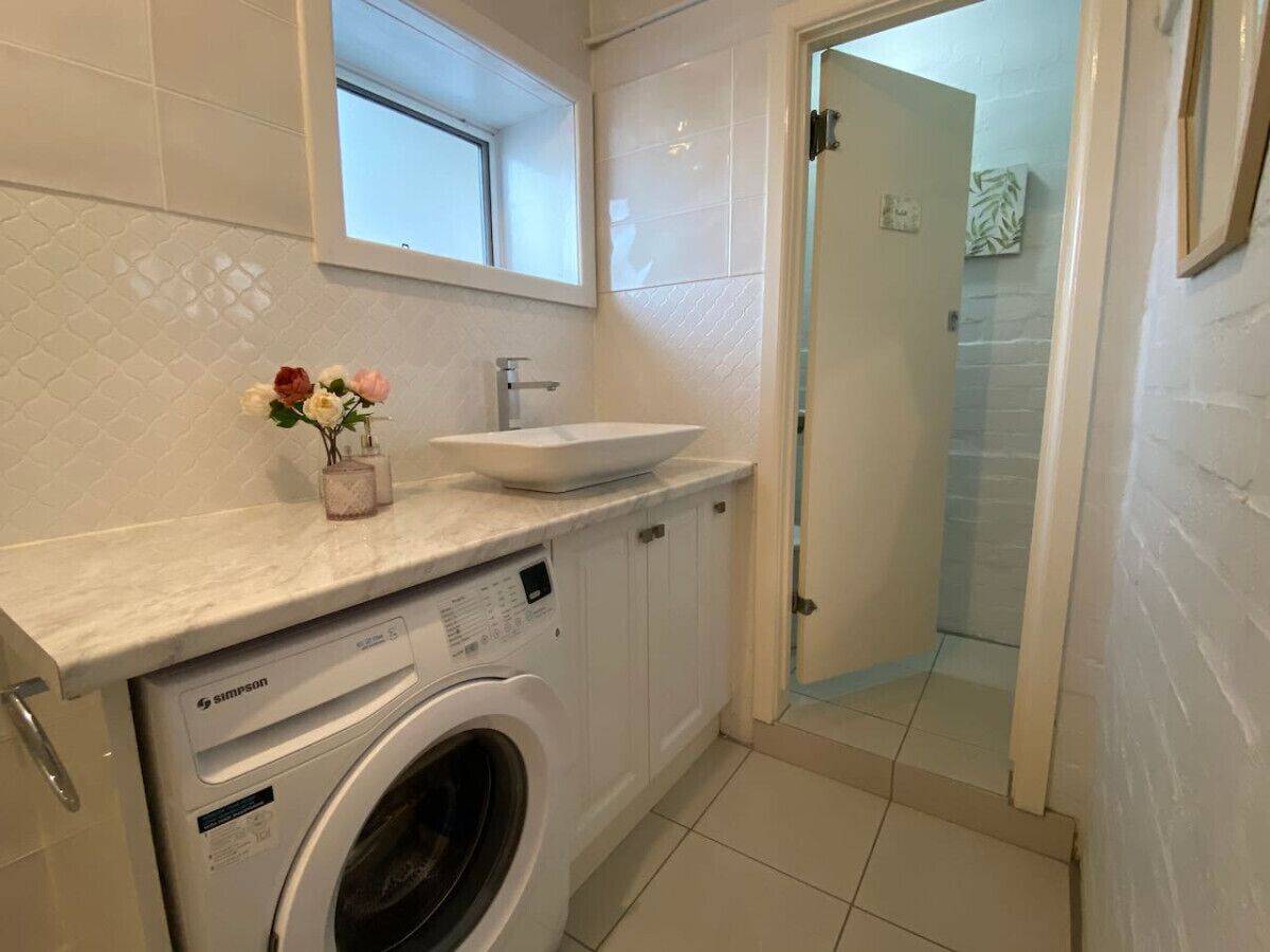 Een kleine wasruimte met een voorlader wasmachine, een wasbak en een klein raam boven het aanrecht.