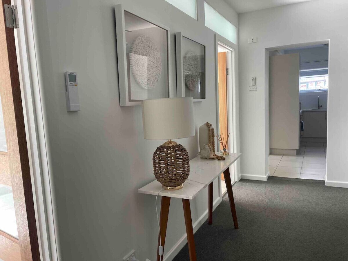 Un couloir avec une console blanche, une lampe et des œuvres d’art encadrées.