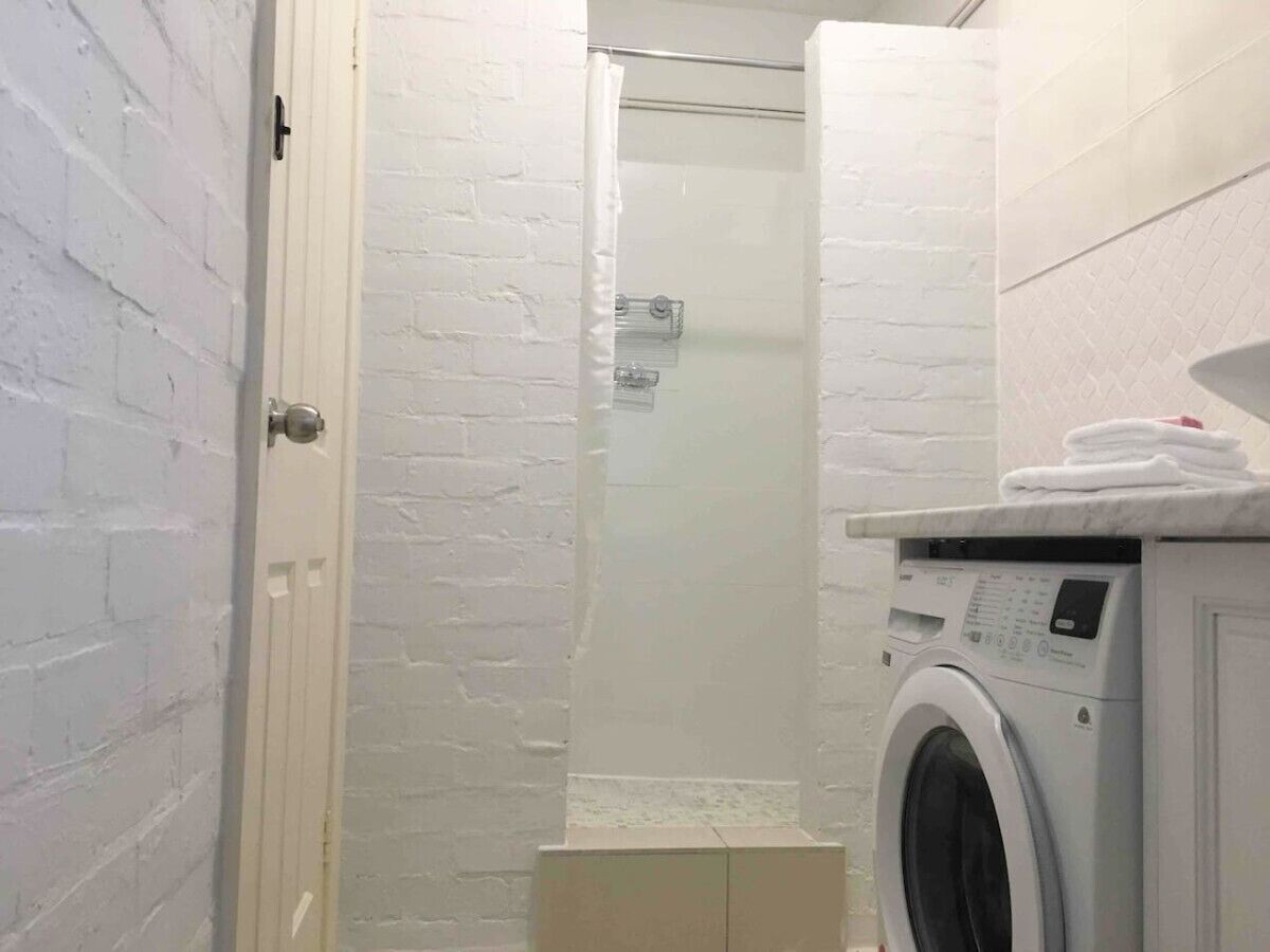 Een kleine wasruimte met een wasmachine, een douche en een deur naar een andere kamer.