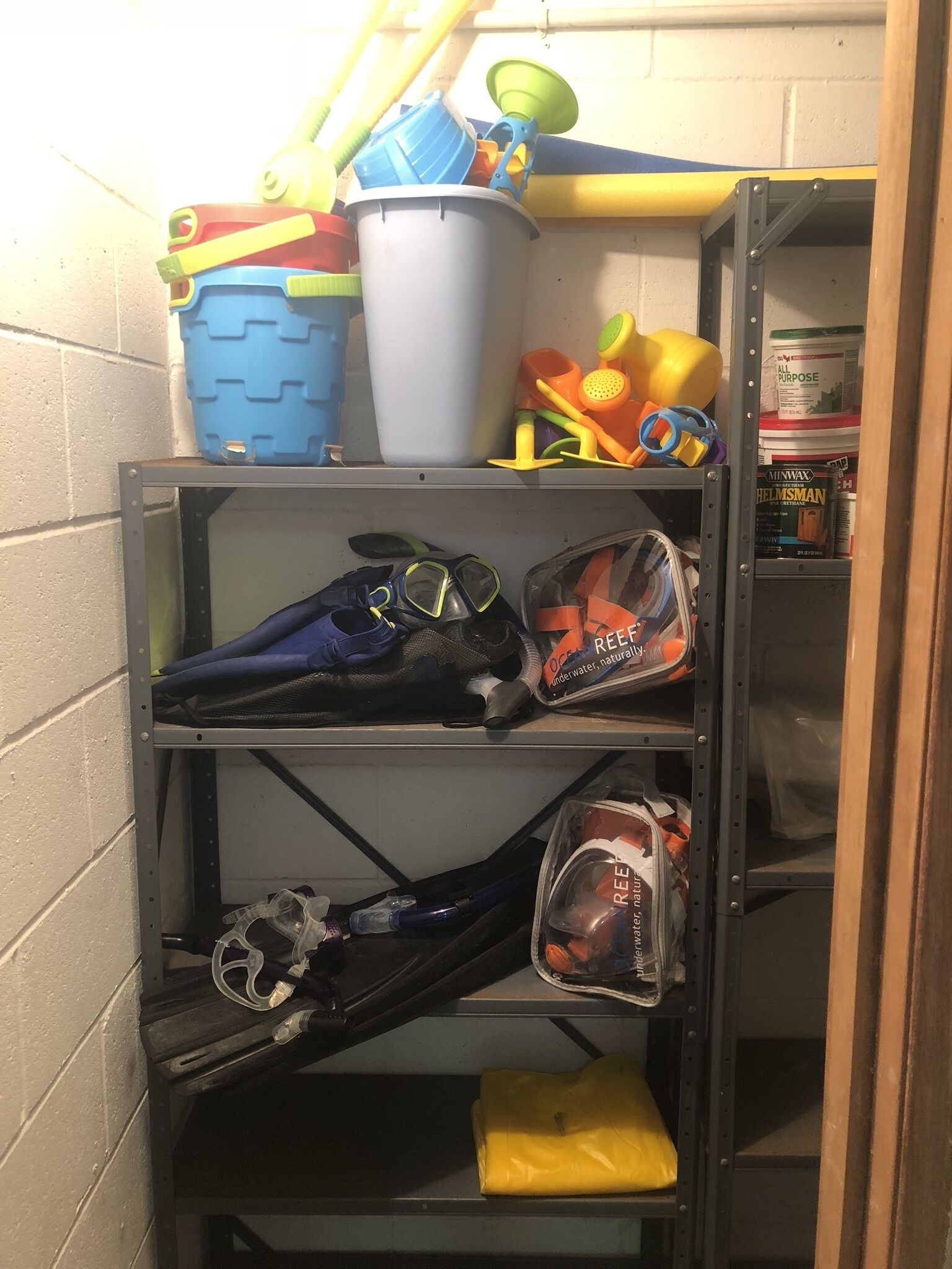 A storage unit with shelves holding various items including a blue bucket, a white bucket, and a bag labeled 'OCEAN REEF'.