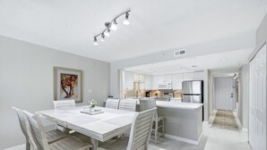 A modern kitchen with white cabinetry, a central island, and a dining area with a white table and chairs.