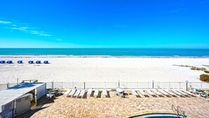 A beach view with a pool area, lounge chairs, and a fenced swimming pool.