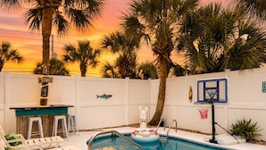 Una piscina con lettini, un canestro da basket e palme.