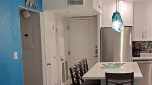 Une cuisine moderne avec des meubles blancs, un réfrigérateur en acier inoxydable et un luminaire suspendu bleu.