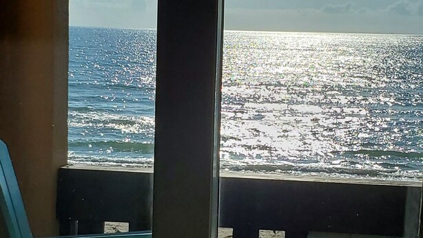 Une vue depuis un balcon avec une porte vitrée, donnant sur une étendue d’eau et un ciel dégagé.