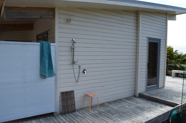 A house with a wooden deck, a small wooden stool, a towel hanging on the railing, and a door leading to a covered porch. - Luxurious Holiday Home (Mangonui)