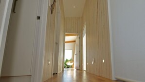 A hallway with wooden flooring and white walls, leading to a room with a large window.