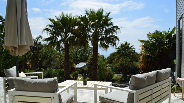 A deck with white furniture, including a sofa and chairs, surrounded by palm trees and a view of the ocean.